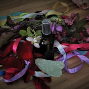 healing fae oil with jade sua sha tool on a wooden table with colorful ribbons