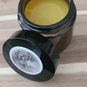small jar of muted yellow healing winter hand salve open on a wooden table